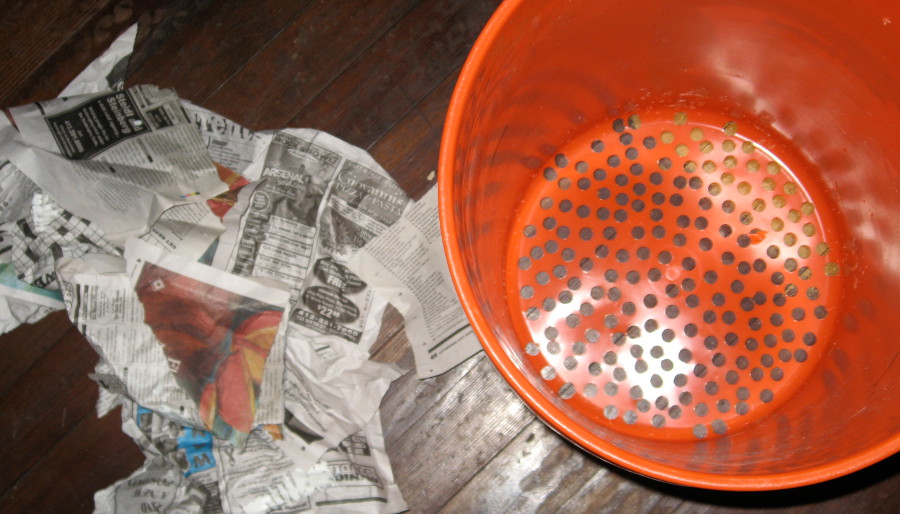 bucket with holes drilled in it and newspaper scraps